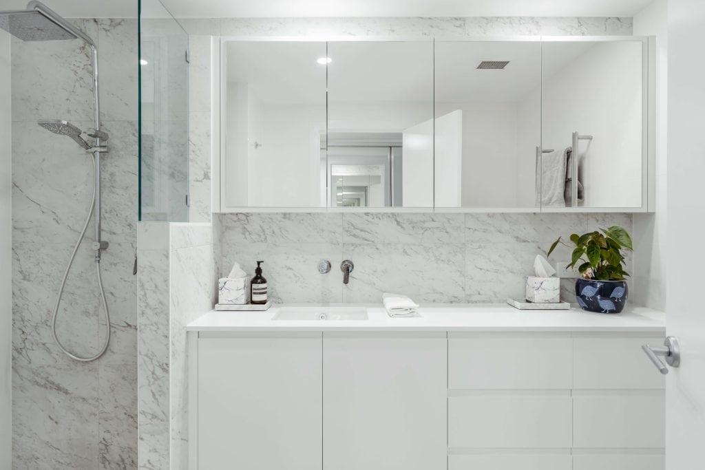 Sleek bathroom featuring marble walls and countertop with a large mirror, glass shower divider, and modern fixtures, in a New Farm, Brisbane home renovation.